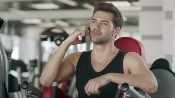 Atleet man praten smartphone na training over sport machine in fitness gym — Stockvideo