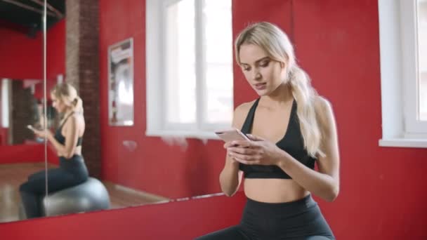 Bella donna utilizzando smartphone nel fitness club. Sorridente donna in forma avendo riposo — Video Stock