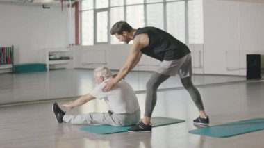 Spor kulübünde yaşlı adama uzanan fitness antrenörü.