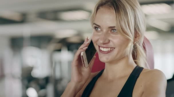 Mooie vrouw praten smartphone in fitness gym. Glimlachend meisje met pauze — Stockvideo