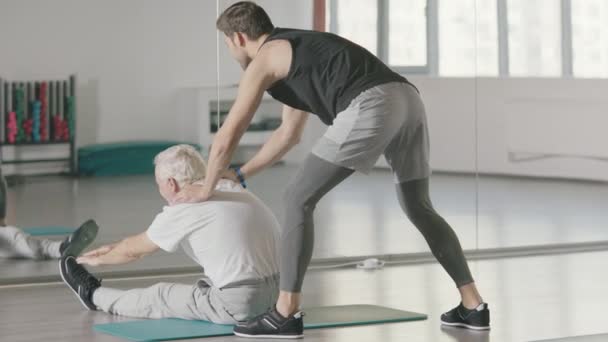 Entraîneur sportif aidant l'homme retraité faire de l'exercice d'étirement dans le club de fitness . — Video