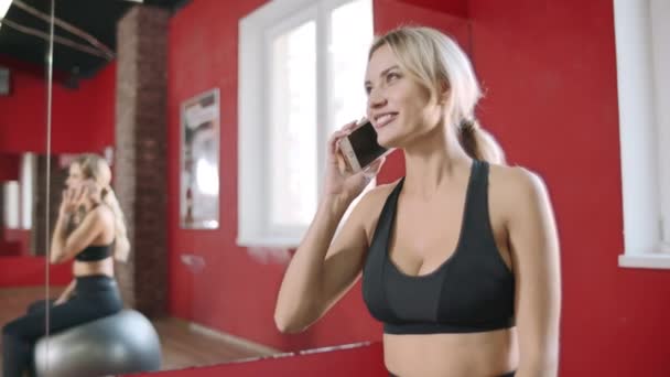 Fitness kadın spor kulübünde cep telefonu arıyor. Spor salonunda oturan genç kadın — Stok video