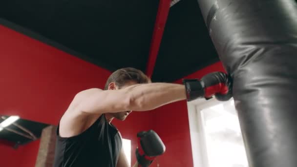 Boxeador hombre pateando bolsa de combate en gimnasio vista de ángulo bajo . — Vídeo de stock