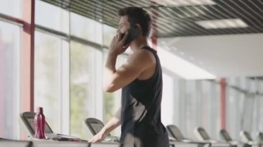 Yakışıklı adam spor salonunda cep telefonu kullanıyor. Koşu bandında koşan güçlü sporcu