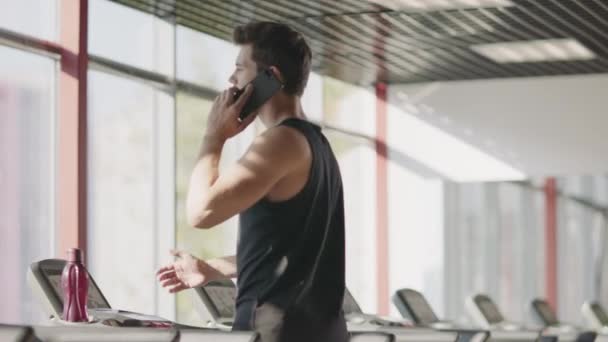 Sportowiec człowiek rozmawia telefon na bieżni w klubie fitness. — Wideo stockowe