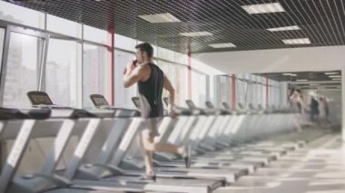 Spor kulübünde koşu bandı makinesinde su içen adam.