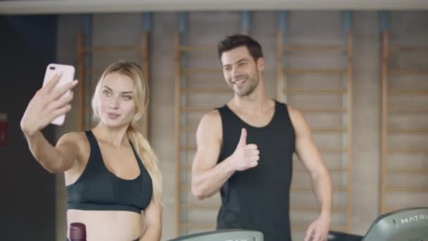 Mujer seria posando foto móvil en el entrenamiento de fitness. Hombre haciendo sí gesto — Vídeos de Stock