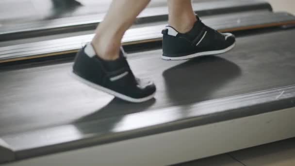 Κοντινό πλάνο στα πόδια που τρέχουν πίσω στον διάδρομο στο γυμναστήριο. — Αρχείο Βίντεο