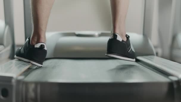 Primer plano de los pies a partir de correr en la cinta de correr en el gimnasio de fitness. Vista posterior de zapatos negros — Vídeo de stock