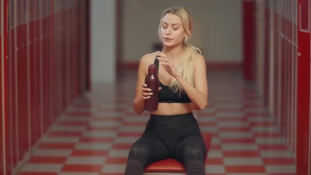 Vermoeide Sportvrouw opening sport fles in kleedkamer. Sexy meisje nippen water — Stockvideo