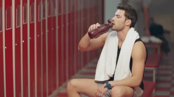 Tired sportsman drinking water in dressing room. — Stock Video