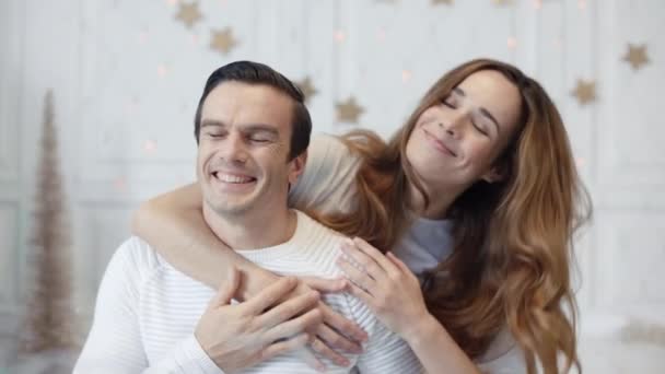 Улыбающаяся жена спрашивает мужа, закрывая глаза. Радостная семья празднует Новый год — стоковое видео