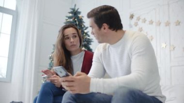 Lüks yatak odasında cep telefonları ile oturan ciddi çift.