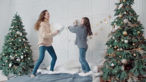 Улыбающиеся мать и дочь играют с подушками в роскошной спальне . — стоковое видео