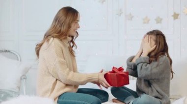 Neşeli kız yatak odasında yeni yıl hediyesi alıyorum. Mutlu anne hediye sunan