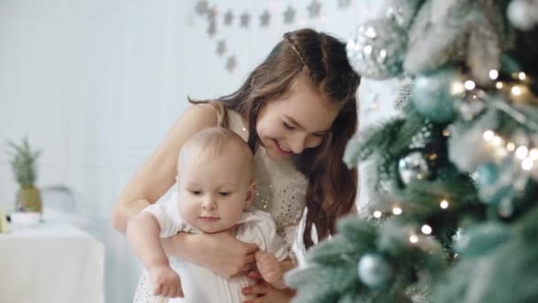 Gros plan fille heureuse tenant enfant près de l'arbre de Noël dans la maison moderne . — Video