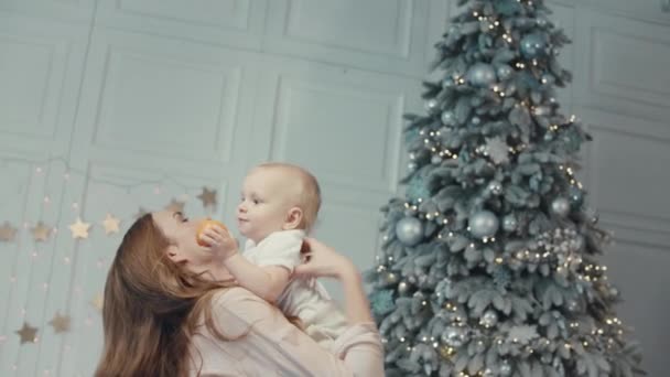 Χαρούμενη μητέρα φιλιά χαριτωμένο παιδί κοντά χριστουγεννιάτικο δέντρο σε μοντέρνο διαμέρισμα. — Αρχείο Βίντεο