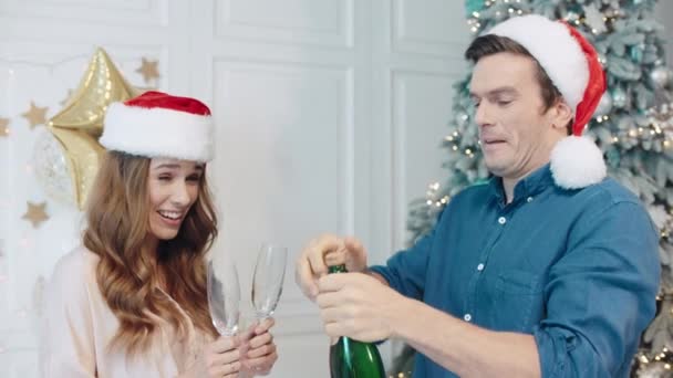 Pareja sonriente celebrando año nuevo con champán en sombreros de santa . — Vídeos de Stock