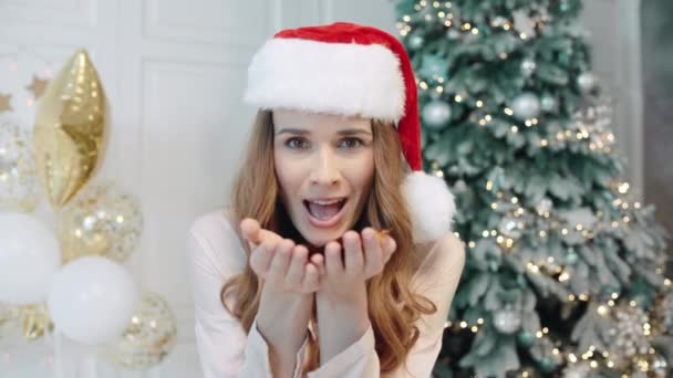 Portrait of happy woman blowing confetti in santa hat. — Stock Video