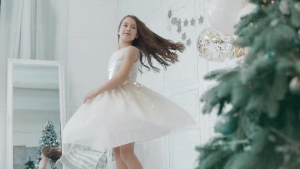 Schönes Mädchen dreht sich in der Nähe des Weihnachtsbaums im weißen Kleid. — Stockvideo