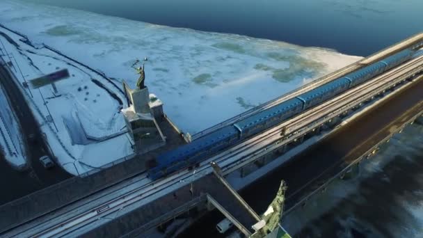 Pociąg Metro porusza się koleją nad mostem samochodowym nad lodowatą rzeką w zimowym mieście — Wideo stockowe