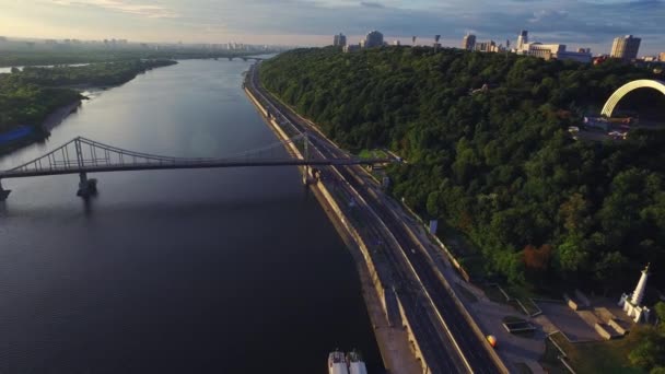 Автомобиль движется по шоссе вдоль реки в летнем городе. Вид с воздуха на достопримечательности города — стоковое видео