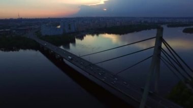 Akşam şehrinde nehir üzerinde asma köprü. Drone görünümü akşam şehir manzara