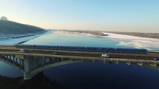 Вид с воздуха поезд метро езда по мосту железной дороги через реку шоссе в зимний период — стоковое видео