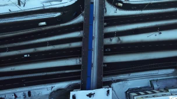 Top View metro trein rijden op brug over besneeuwde snelweg in winter City — Stockvideo