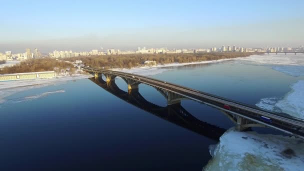 Вид з повітря на автомобільний міст через замерзлу річку в зимовому місті. Відкриті залізниці метро — стокове відео