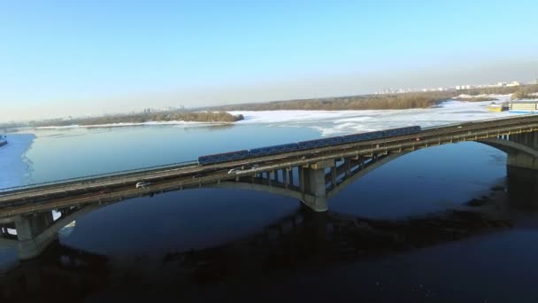 Этро-поезд с видом на дрон катается по мостовой железной дороге зимой. Автомобильное движение по шоссе — стоковое видео