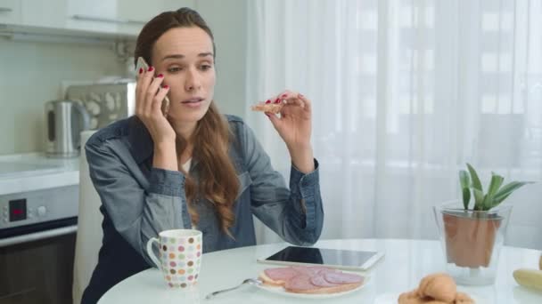 Nő beszél telefonon evés közben reggelizni. Lány eszik ízletes szendvicset — Stock videók