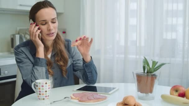 Leende kvinna pratar på telefon. Hemmafru äter sadwich och kaffe hemma. — Stockvideo