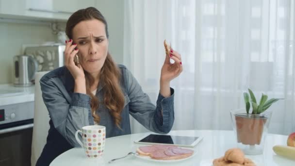 Mujer seria que tiene una llamada telefónica desagradable sentado en la cocina . — Vídeos de Stock