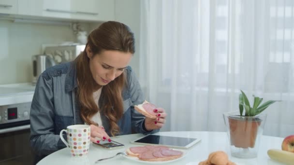 Lachende vrouw praten smartphone tijdens het ontbijt in moderne keuken. — Stockvideo