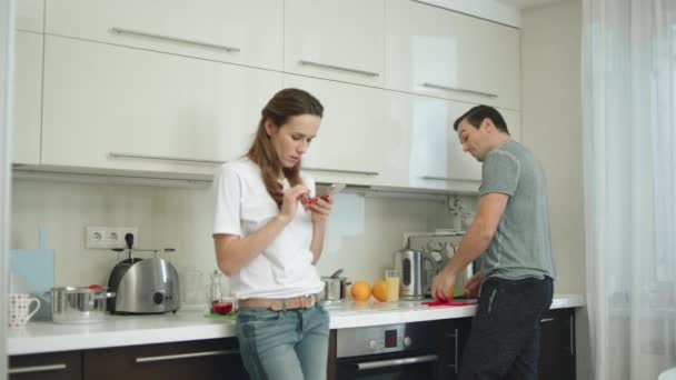 Feliz pareja cocinando el desayuno en la cocina moderna. Mujer sonriente tomando fotos — Vídeo de stock