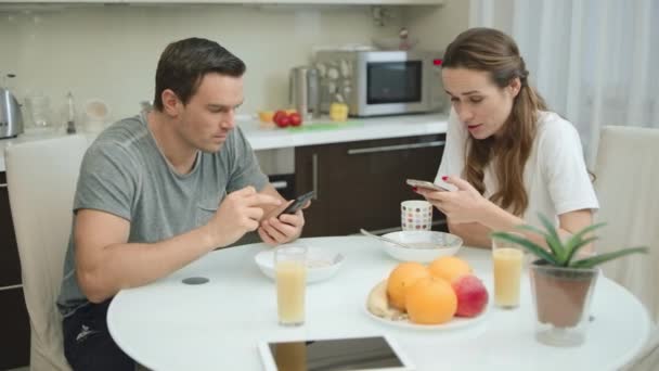 Pareja feliz mirando teléfonos móviles durante el desayuno saludable . — Vídeos de Stock