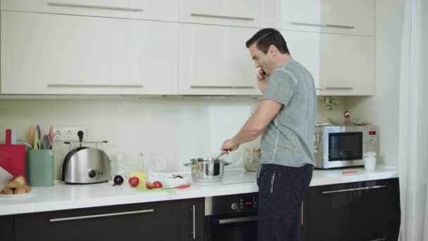 Lächelnder Mann kocht gesundes Abendessen in moderner Küche. — Stockvideo