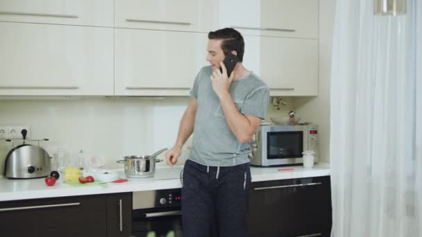 Homem sorridente cozinhando jantar saudável em casa. Feliz homem de negócios falando telefone — Vídeo de Stock