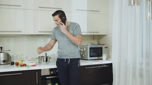 Um homem zangado a falar ao telefone na cozinha. Agressivo homem balançando braços — Vídeo de Stock