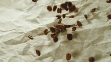 Kavrulmuş kahve çekirdekleri ağır çekimde ahşap masa yüzeyine düşüyor..