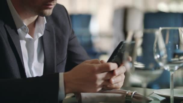 Hombre de negocios sonriente leyendo buenas noticias en el teléfono inteligente en el restaurante — Vídeos de Stock