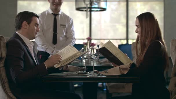 Menu de leitura feliz casal no restaurante. Pessoas de negócios escolhendo comida no café — Vídeo de Stock