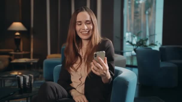 Szczęśliwa kobieta za pomocą smartfona do rozmowy wideo online w hotelowym salonie — Wideo stockowe