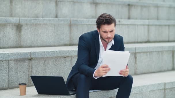 Бізнесмен читає бізнес-документи на вулиці. Занепокоєний чоловік сидить на сходах — стокове відео