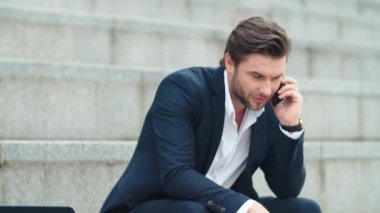 İş adamı şehirde akıllı telefondan konuşuyor. Erkek çalışan zaferi kutluyor