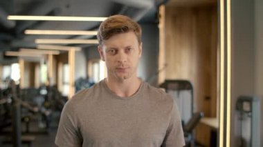 Spor kulübünde baş parmağını gösteren ciddi bir fitness adamı. Sporcu spor salonunda duruyor.