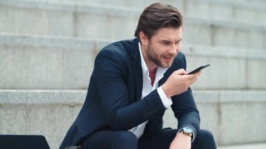 İş adamı cep telefonundan sesli mesaj kaydediyor. Merdivenlerde oturan adam.