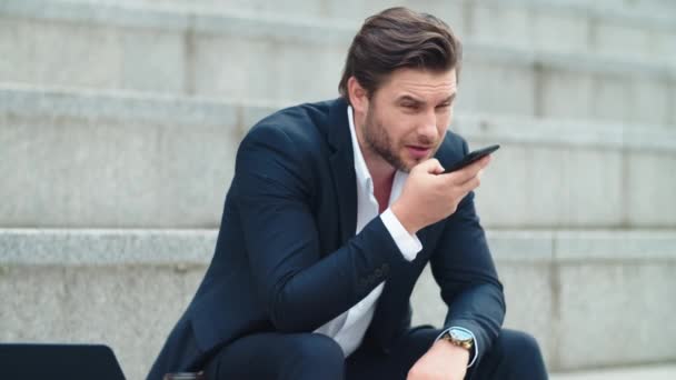 Geschäftsmann, der Sprachnachrichten auf seinem Handy in der Stadt aufzeichnet. Mann sitzt auf Treppe — Stockvideo
