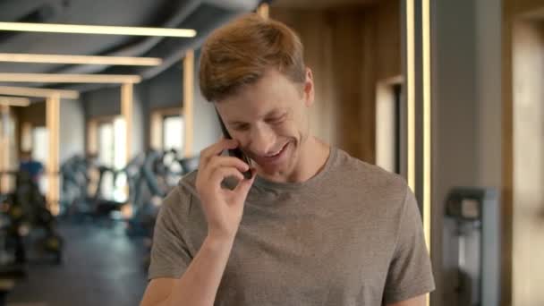 Homem de fitness alegre usando telefone no clube desportivo. Fisiculturista de pé no ginásio . — Vídeo de Stock